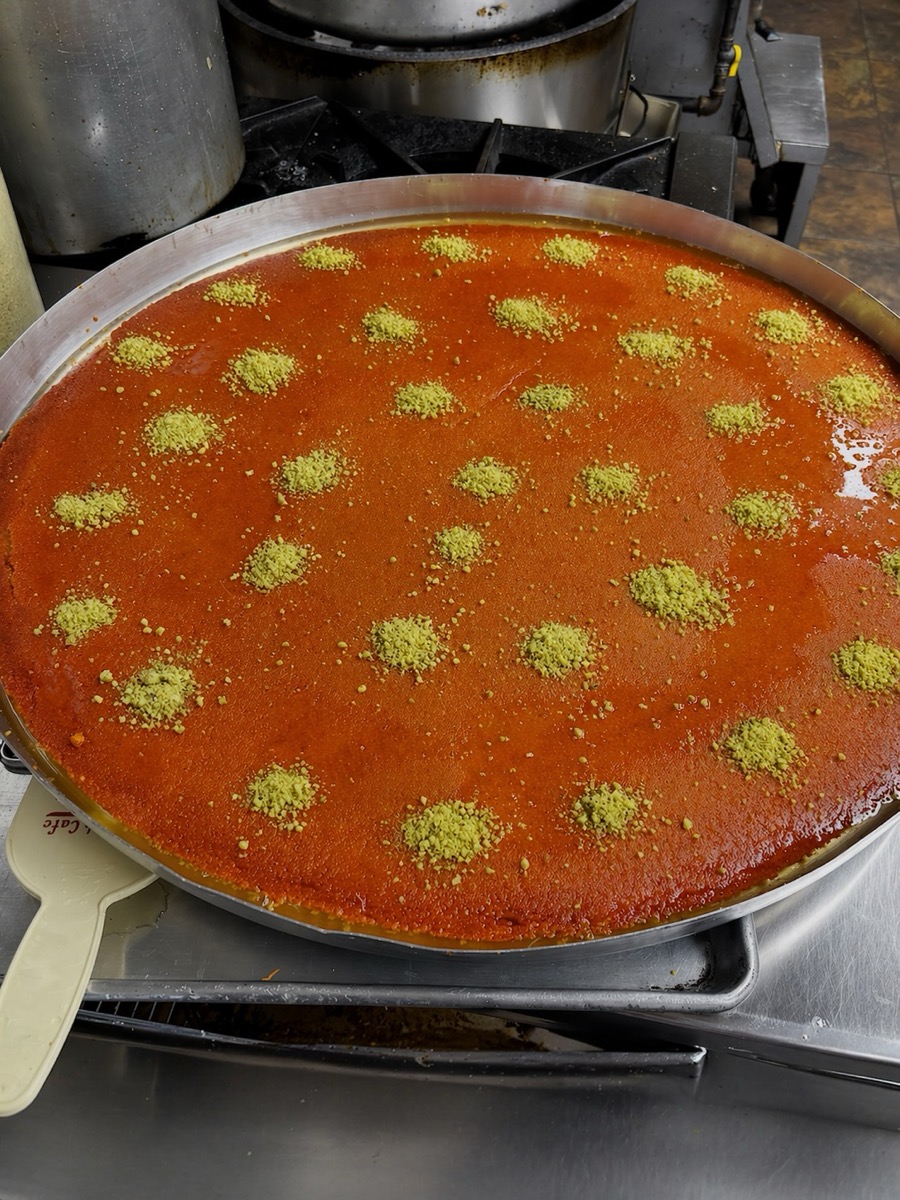 Knafeh being pulled apart showing a dramatic cheese pull with golden syrup dripping